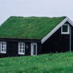 Charming black wooden house with a grass roof in the tranquil Faroe Islands landscape.